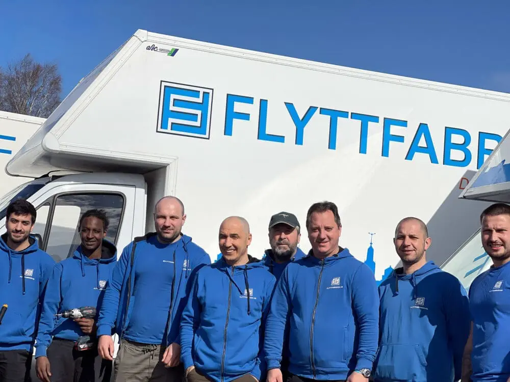 Sex glada flyttgubbar i blå tröjor från Flyttfabriken redo att utföra en bohagsflytt i Stockholm.