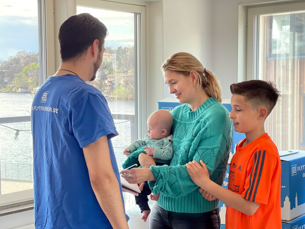 Resultatet av en lyckad bohagsflytt i Stockholm: en glad barnfamilj i sitt nya hem pratar med en flyttgubbe i blå tröja.