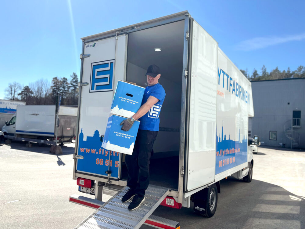 En anställd i Flyttfabrikens blå tröja bär ombord två matchande blå flyttkartonger på en lastbil på väg till magasinering i anslutning till en flytt i Stockholm.