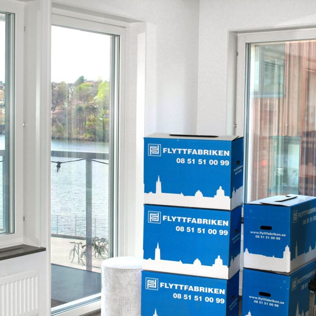 Flyttmaterial i form av Flyttfabrikens blå flyttkartonger, prydligt staplade i ett hem med sjöutsikt.